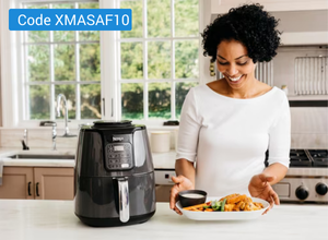 Frau in weißem Oberteil steht in moderner Küche vor schwarzer Heißluftfritteuse und hält Teller mit frittiertem Essen und Dip-Schale.