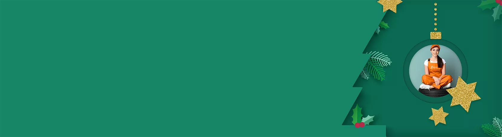 Frau in oranger Latzhose und weißem T-Shirt sitzt mit verschränkten Beinen auf einem Stapel Autoreifen vor grünem Hintergrund.