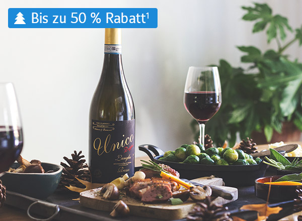 Flasche Rotwein mit goldener Kapsel und schwarzem Etikett 'Unico', daneben Weinglas mit Rotwein, grüne Trauben und Tannenzapfen auf Tisch.