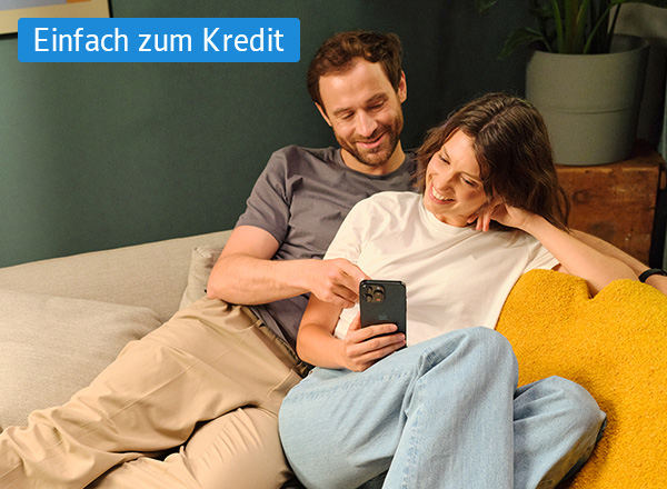 Zwei Personen sitzen entspannt auf einem Sofa, eine hält ein Smartphone, im Hintergrund steht ein Blumentopf auf einem Holzmöbel.