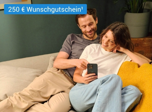 Zwei Personen sitzen entspannt auf einem Sofa, eine hält ein Smartphone, im Hintergrund steht ein Blumentopf auf einem Holzmöbel.