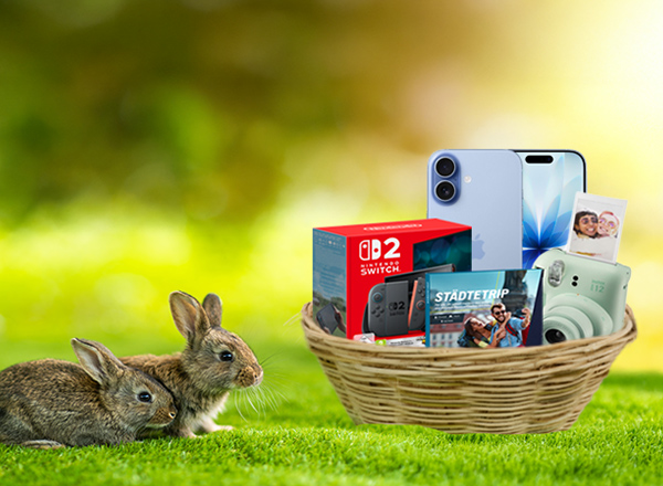 Zwei Hasen im Gras neben einem Korb mit Technikgeschenken und Kamera im Frühling