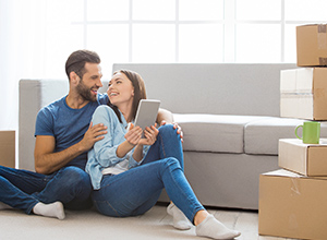 Mietkautionsversicherung: junges Paar sitzt auf dem Fussboden ihrer neuen Wohnung